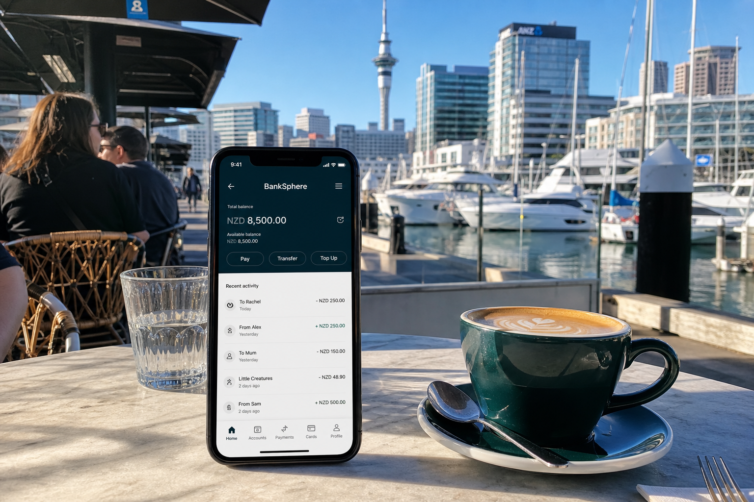 Sunny Auckland waterfront with a smartphone showing an original banking balance and transfers