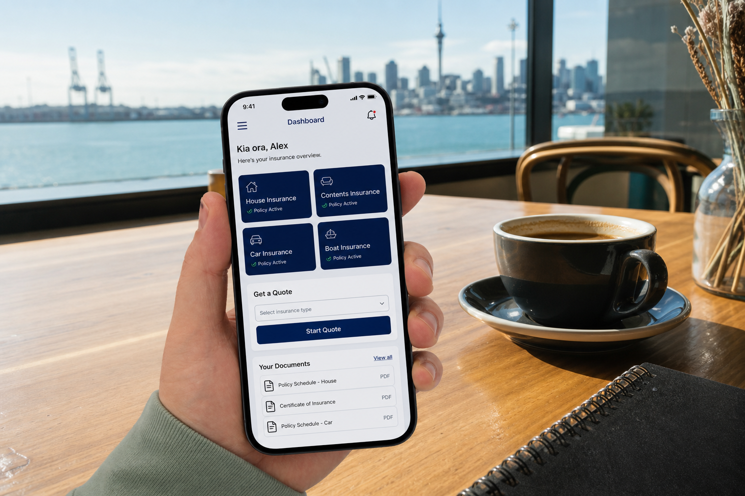 Sunny Auckland cafe with a phone showing an original insurance policy and quote dashboard