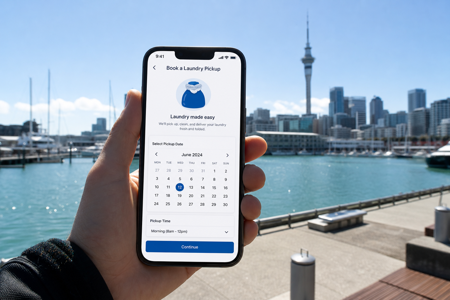 Sunny Auckland waterfront with a smartphone showing a laundry pickup booking screen