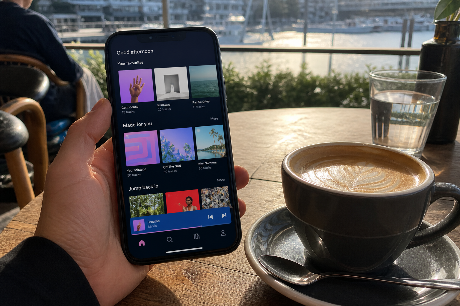Sunny Auckland cafe with a phone showing an original music player, playlist and artist cards